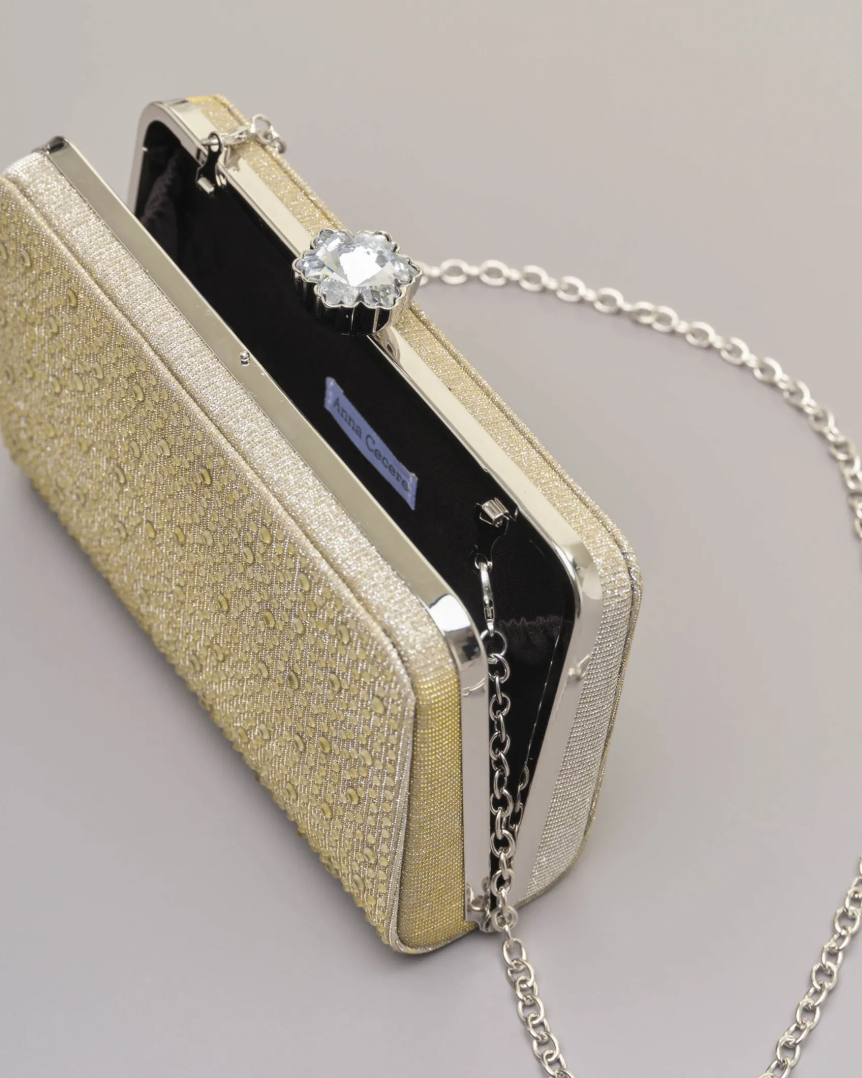 Clutch rigida color oro in lurex con strass tono su tono applicati sul davanti e chiusura a gioiello a scatto